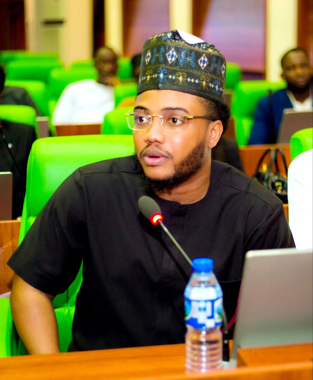 Harrison speaking at formal conference wearing traditional Nigerian cap