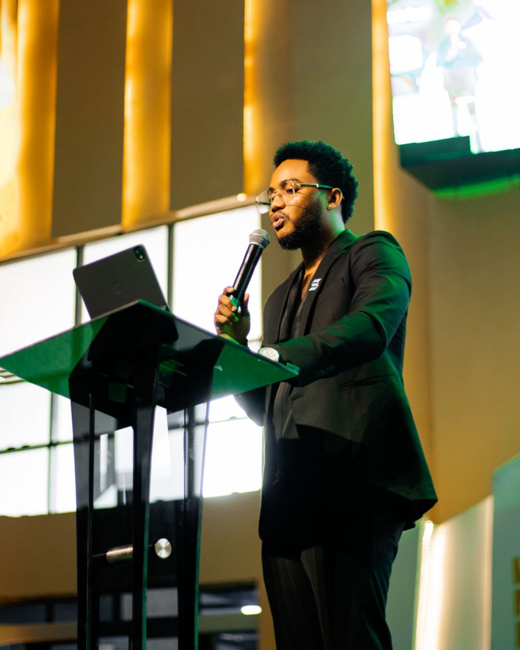 Harrison speaking at podium with golden stage lighting